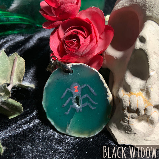 A black widow spider is hand-painted on a circular green agate slice.