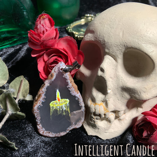 A yellow candle, representing intelligence glows on a gray, teardrop-shaped agate slice pendant.