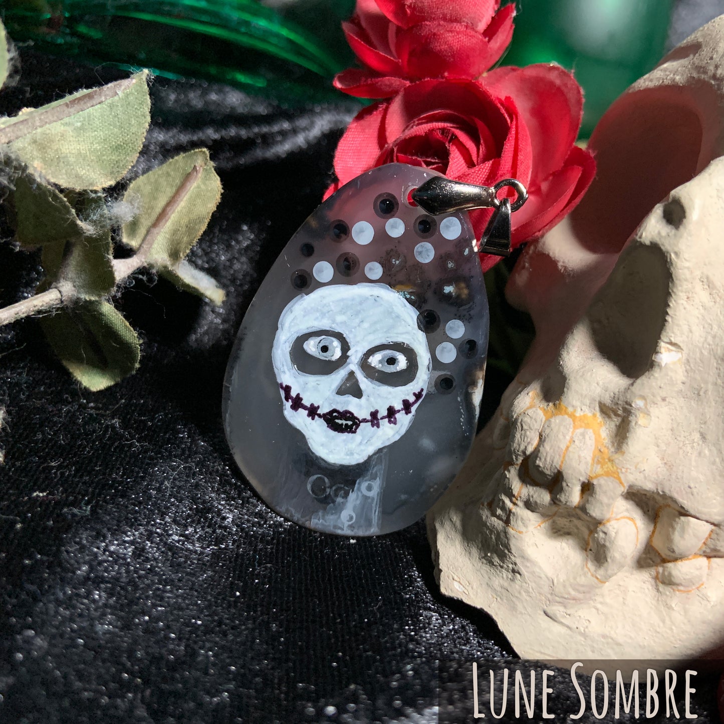 A woman with skull make-up and an otherworldly quality is hand-painted on a tear-drop shaped, translucent gray agate slice. Everything is painted in black, white, and gray.